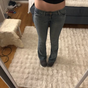 Blå bootcut jeans från weekday  - Säljer ett par ljusblå jeans från weekday med bootcut passform och låg midja. Jeansen har klassiska fem fickor, snygga slitningar och en dekorativ patch bak i linningen. Tillverkade i mjukt denimtyg för en bekväm känsla.