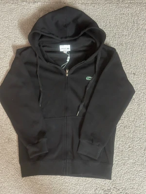 Lacoste hoodie - Säljer min svarta Lacoste-tröja. Fin passform och skönt material. Tröjan är i fint skick utan hål eller fläckar. Pris kan diskuteras vid snabba köp.