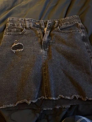 Svart jeanskjol från UNIQ Ullared! - Säljer en svart jeanskjol från UNIQ Ullared med kant nertill och slitning på framsidan. Kjolen har dragkedja framtill. Perfekt för dig som gillar en avslappnad stil.