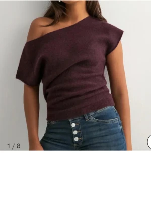 Vinröd oneshoulder topp - Säljer en vinröd oneshoulder topp i mjukt stickat material. Toppen har en asymmetrisk halsringning som går över ena axeln och sitter tajt i midjan. Perfekt att styla med jeans eller kjol för en trendig look.