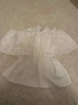Vit offshoulder blus från Gina Tricot - Säljer en superfin vit offshoulder blus från Gina Tricot i storlek S. Blusen har volangdetaljer och är tillverkad i ett lätt, luftigt material som ger en romantisk vibe. Perfekt till sommaren och passar snyggt till både jeans och kjol.