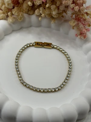 Elegant tennisarmband för en tidlös look - Detta exklusiva tennisarmband i rostfritt stål, pläterat med 18K guld, är skapat för dig som uppskattar enkel elegans. Armbandet är dekorerat med gnistrande zirkonstenar som ger ett lyxigt uttryck. Det är dessutom vattentåligt och behåller sin lyster även vid daglig användning.  📏 Längd: 17 cm – sitter bekvämt och stilrent på handleden.  Perfekt som en diskret detalj till vardagen eller som ett elegant smycke vid speciella tillfällen 💛  🛍️ Lägg till en touch av elegans i din smyckessamling redan 