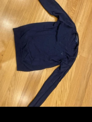 Mörkblå V-ringad tröja från Gant - Snygg mörkblå V-ringad tröja från Gant i premium bomull. Klassisk och stilren modell med långa ärmar och diskret logga på bröstet. Perfekt till jeans eller chinos för en clean look.