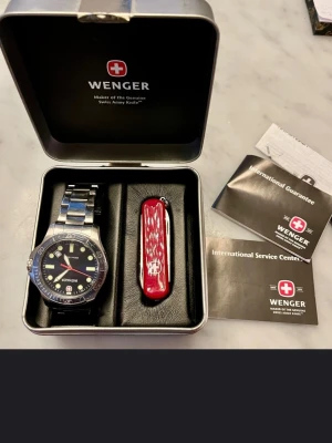 Wenger Swiss Military med schweizisk armékniv  - Wenger militärklocka med schweizisk armékniv.  Vattentät 100 meter, datum, boett I massivt stål, kommer med box i stålplåt, garantikort och kvitto. 