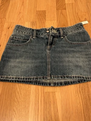 Jeanskjol från Hollister med broderi - Säljer en blå jeanskjol från Hollister med snygga broderade blommor på bakfickorna. Kjolen har klassisk femficksdesign, bälteshällor och kontrastsömmar. Perfekt för dig som gillar en chill och trendig stil. Aldrig andvänd(köpt för runt 420kr)