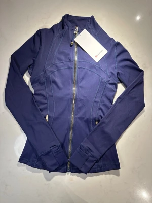 Lululemon Define Luon mörkblå träningsjacka Strl.  XS - vinted tag - oanvänd - Hej! Jag säljer en Lululemon Define träningsjacka i svart färg i mycket bra skick - storlek XS Jackan har hel dragkedja samt hög krage Mjukt och stretchigt material - perfekt för träning, gym eller yoga Kommer från ett djur- och rökfritt hem Skickad alltid inom någon timme efter köp!
