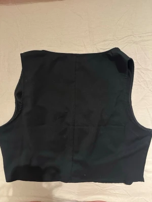 Svart korsettopp från H&M Divided XL - Säljer en svart korsettliknande topp från H&M Divided i storlek XL. Toppen har v-ringning och knäppning med svarta knappar framtill. Modellen är ärmlös och har en figurnära passform som ger en snygg siluett. Haf aldrig använts, köptes från H&M.