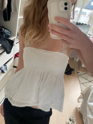 Vit smockad axelbandlös tröja - Söt vit topp med smockad överdel och volangig nederdel. Jätte fin för varma dagar och enkel att styla med jeans eller kjol. Jag är 167cm.