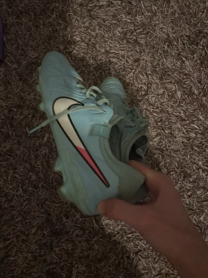 Ljusblå Nike fotbollsskor - Säljer ett par ljusblå Nike fotbollsskor med klassisk snörning och rund tå. Skorna har en vit och svart swoosh-logga på sidan och dobbar under sulan för bra grepp på planen. Ovandelen är i syntetmaterial och insidan är fodrad i rött.