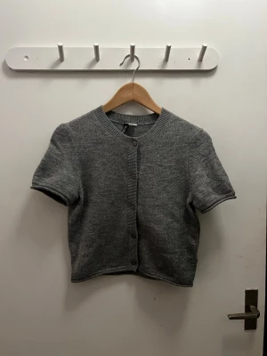 Grå kortärmad kofta från H&M Divided - Kortärmad grå kofta från H&M Divided i mjukt stickat material. Klassisk rund halsringning och knappar.💓💓