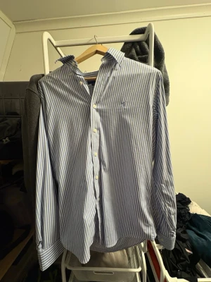 Blårandig skjorta från Ralph Lauren - Säljer en klassisk blårandig skjorta från Ralph Lauren Performance i storlek M. Skjortan har vit knappstängning, button down-krage och den ikoniska broderade loggan på bröstet. Tillverkad i bomull för en skön och luftig känsla.