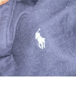 Mörkblå pikétröja Polo Ralph Lauren S - Klassisk mörkblå pikétröja från Polo Ralph Lauren i storlek S. Tröjan har korta ärmar, krage och två knappar framtill. Ikoniska vita broderade loggan på bröstet. Tillverkad i mjuk bomull som känns skön mot huden.
