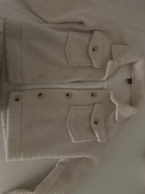 Beige teddyjacka med fickor - Mysig beige teddyjacka från shein med stora bröstfickor och knappar framtill. Jackan har en klassisk krage och är gjord i mjukt teddy-material som håller dig varm. Perfekt för dig som vill ha en trendig och bekväm look.