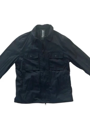 Svart vindjacka från Bomboogie, S - Svart vindjacka från Bomboogie i storlek S. Jackan har två stora bröstfickor med knappar, dragkedja framtill och klassisk krage. Materialet är vattenavvisande, perfekt för blåsiga dagar. Enkel och stilren design som funkar till det mesta. Nypris ca 2700kr | Pris kan diskuteras!