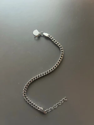 Snygg silverfärgad kedjearmlänk - Stilren armlänk i silverfärg med klassisk kedjedesign och justerbar längd. Länken har en liten rund bricka vid låset och passar perfekt för dig som gillar minimalistiska accessoarer. Enkel att matcha med andra smycken och funkar året runt.
