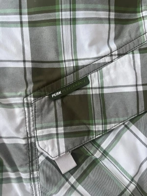 Rutiga Peak Performance shorts - Säljer ett par gröna och vita rutiga shorts från Peak Performance. De har flera praktiska fickor, bälteshällor och stängs med dragkedja och knapp. Perfekta för sommardagar och har en avslappnad passform.