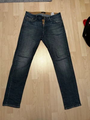 Mörkblå jeans från Jack & Jones - Säljer ett par mörkblå jeans från Jack & Jones i klassisk femficksmodell. Jeansen har raka ben, normal passform och snygga slitningar framtill för en avslappnad look. Tillverkade i slitstarkt bomullsmaterial och perfekta till vardagsstilen. Modellen är Tapered Mike. 