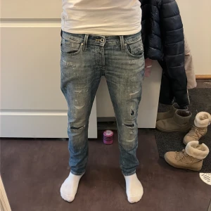jack and jones - Säljer ett par blå jeans från jack and jones med slitningar. Jeansen har skinny passform, normal midja och coola färgstänk för en extra edge. Klassisk femficksmodell i jeansmaterial och snygg tvättad look.