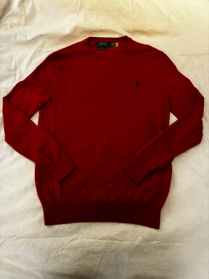 Röd merinoullströja Polo Ralph Lauren - Snygg röd tröja från Polo Ralph Lauren i mjuk merinoull. Klassisk rund halsringning, diskret broderad logga på bröstet och långärmad modell. Perfekt till jeans eller chinos för en clean och stilren look.