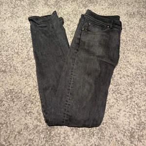 Mörkgrå jeans från Tiger of Sweden - Snygga mörkgrå jeans från Tiger of Sweden med klassisk femficksdesign och diskret logga vid myntfickan. Jeansen har raka ben och slim passform, tillverkade i mjukt jeanstyg som sitter skönt hela dagen. Liten slitning på knät, och litet hål i bakfickan. 