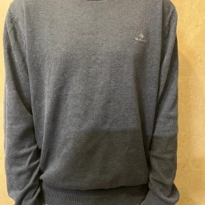 Mörkblå stickad tröja från GANT - Snygg mörkblå stickad tröja från GANT med diskret logga broderad på bröstet. Tröjan har rund hals, ribbade muddar vid ärmslut och nederkant samt långärmad passform. Perfekt för dig som gillar klassisk och stilren design. Sitter som s. 