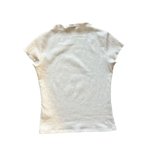 Vit  topp - Lindex - Toppen har en slim passform och är tillverkad i ett mjukt, stretchigt material som sitter snyggt på kroppen. Perfekt att matcha med jeans eller kjol för en clean look.