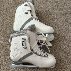  skridskor Reebok - Snygga vita skridskor från Reebok med grå detaljer och broderat mönster på sidorna. De har snörning och mjuk grå fuskpäls runt skaftet för extra komfort och stil. Perfekta för vinterns isäventyr.