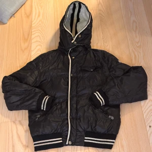 Svart pufferjacka från Moncler - Är i OK skick, dragkedjan för att stänga jackan är trasig men går att stänga med knapparna, samt ena fickan är dragkedja trasig. Dunet har börjat klumpa ihop sig. Osäker på om jackan är äkta eller inte. Vid frågor är det bara att höra av sig