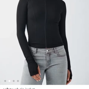 Svart slim zip-jacka med lång ärm - Svart, figurnära zip-jacka med lång ärm och tumhål. Jackan har en minimalistisk look med hel dragkedja framtill och är tillverkad i ett mjukt, stretchigt material som sitter tight mot kroppen. Perfekt för en clean och sportig stil.