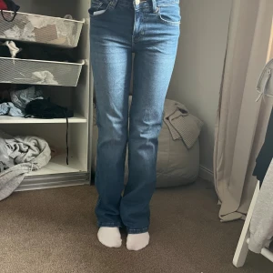 Blå bootcut jeans  - Säljer ett par klassiska blå jeans med bootcut-modell. Jeansen har snygga bakfickor med lock och silverfärgade knappar. Perfekta för dig som gillar en tidlös och trendig look. Materialet är jeans