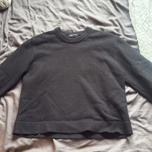 Svart stickad tröja från Monki - En svart stickad tröja från Gina med rund hals och ribbade muddar vid hals, ärmslut och nederkant. Tröjan har en enkel och clean look med lång ärm och normal passform, perfekt för att hålla sig varm under kyliga dagar.