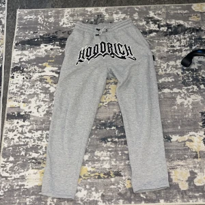 Grå mjukisbyxor från Hoodrich XS - Snygga grå mjukisbyxor från Hoodrich i storlek XS med stor svart och vit logga framtill. Byxorna har snörning i midjan och är gjorda i mjukt bomullsmaterial. Perfekta för chill och streetwear-stil.