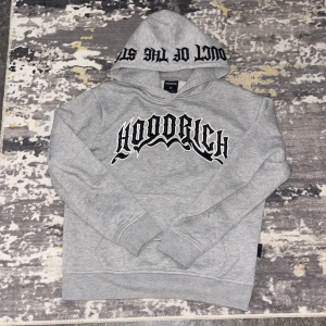Grå hoodie från Hoodrich XS - Snygg grå hoodie från Hoodrich i storlek XS med svart broderad logga på bröstet och text på huvan. Tröjan har en klassisk loose passform, långärmade ärmar och är tillverkad i mjuk bomullsmix med fleece på insidan. Perfekt för chill och streetwear.