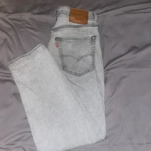 Grå Levi's 511 jeans slim fit - Snygga grå Levi's 511 jeans med klassisk femficksdesign och brunt läderpatch bak. Jeansen har en slim passform och raka ben, tillverkade i mjukt jeanstyg med en ljusgrå tvätt. Perfekt för dig som gillar stilrena och moderna jeans.