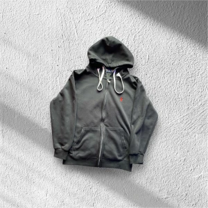 Svart hoodie från Polo Ralph Lauren - Svart hoodie från Polo Ralph Lauren med dragkedja, vit snörning i huvan och röd broderad logga på bröstet. Mjuk bomullskvalitet och känguruficka framtill. Perfekt för chill dagar eller när du vill ha en clean streetstyle.