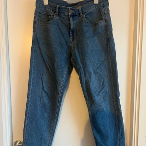 Blå jeansbyxor W34 L34 - Snygga blå jeansbyxor i klassisk modell med raka ben och fem fickor. Jeansen har kontrastsömmar och normal passform, perfekta till vardagslooken. Tillverkade i tåligt denimtyg för en tidlös stil.