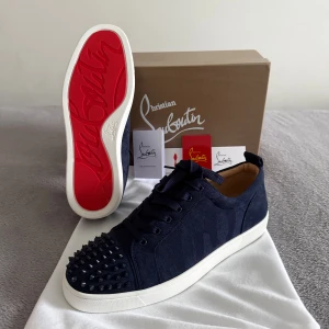 Christian Louboutin skor - Snygga marinblå sneakers från Christian Louboutin i mocka med klassisk röd sula och svarta nitar på tån. Skorna har rund tå, snörning och vit platt sula. Perfekta för dig som vill sticka ut med exklusiv design och edgy detaljer.