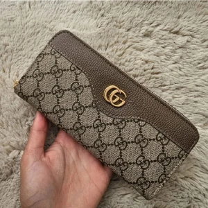 plånbok med GG-mönster - Snygg plånbok i beige och brunt med klassiskt GG-mönster och guldfärgad logga framtill. Plånboken har dragkedja runtom, flera fack för kort och mynt samt detaljer i skinn. Perfekt för dig som vill ha både stil och funktion.