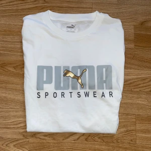 Vit Puma t-shirt med guldlogga - Vit t-shirt från Puma med tryckt logga i guld & grå i storlek S, knappt använd legat i garderoben ett tag nu