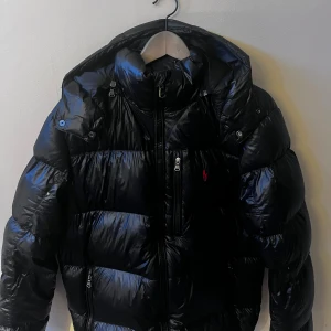 Ralph Lauren Glozzy|M - Tja, säljer nu min Ralph Lauren jacka i ”glozzy” look. Denna jacka är varm och skön med stiligt glans. Perfekt vinterjacka. 9/10 skick förutom på tvättlappen där den rivits upp men inte skadat jackan. Köpt på johnells hemsida för ett år sedan, kvitto medföljer🍾🥂