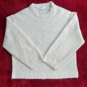 Vit stickad tröja från Gina Tricot - Mysig och stilren tröja i ullblandning med rund hals, ribbade muddar vid ärmslut och nederkant samt långärmad passform. Perfekt för dig som gillar enkel och clean stil med lite fluffig känsla. Aldrig använd – i perfekt skick