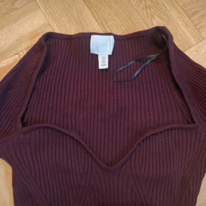 Vinröd ribbad långärmad topp - Säljer en vinröd långärmad topp från Bershka med ribbad struktur och markerad sweetheart-formad söm vid bysten. Toppen är slim fit och har en mjuk, stretchig känsla som sitter snyggt på kroppen. Perfekt för dig som gillar stilrena detaljer och mörka färger.