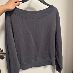 Mörkgrå sweatshirt med bred krage - En stilren mörkgrå sweatshirt med bred ribbad krage och långa ärmar. Tröjan har en loose passform och är tillverkad i mjuk bomull, perfekt för chill dagar. Enkel design utan mönster eller detaljer, passar dig som gillar minimalistisk stil.