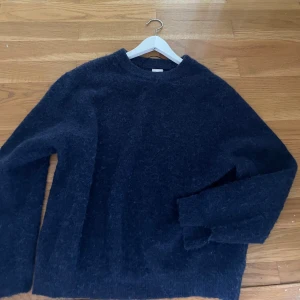 Mörkblå fluffig stickad tröja - Mysig mörkblå stickad tröja med fluffig känsla och rund hals. Perfekt för kyliga dagar och enkel att matcha med jeans eller kjol. Långärmad och i en loose passform för extra komfort.