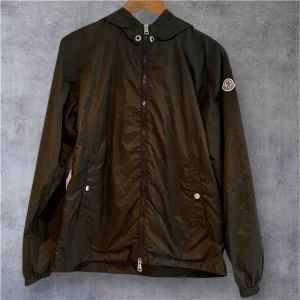 Moncler Windbreaker Size S - Mörkgrön windbreaker från Moncler i mycket fint skick. Den är i storlek 1 i monclers storlek, vilket motsvarar storlek S. Den är i utmärkt skick, inga tecken på användning. Den har en NFC när man scannar Moncler märket, samt en qr kod inne i jackan. Skriv för fler bilder (kan max ta 5 på Plick). Hör av dig om du undrar något!