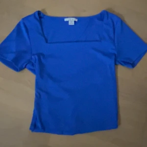 Blå topp med fyrkantig hals från Amisu - Snygg blå topp från Amisu i storlek S med korta ärmar och en modern fyrkantig halsringning. Toppens material är mjukt och stretchigt, perfekt för att skapa en clean och fräsch look. Passar dig som gillar stilrena och färgstarka plagg.