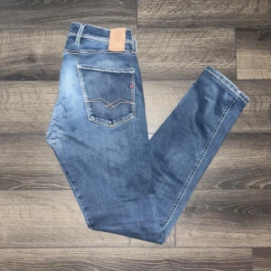 Replay Anbass hyperflex jeans  - Snygga Replay Anbass jeans i blå tvätt med coola slitningar och klassiska detaljer. Slim fit-modell. OBS jeansen har ett litet hål i grenen som syns på sista bilden, de har även ett hål på vänster ben som jag ej vet om det är mode heller defekt! Midja 38cm, längd 102cm. JAG SKICKAR INGA FLER BILDER PÅ NÄR JAG BÄR JEANSEN:) 18