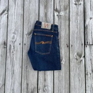 Mörkblå jeans från Nudie Jeans - Snygga mörkblå jeans från Nudie Jeans med klassisk orange söm och ikonisk bakficka. Modellen har smal passform och raka ben. Storlek W28 L32! Defekter syns på bild 3 och 4!