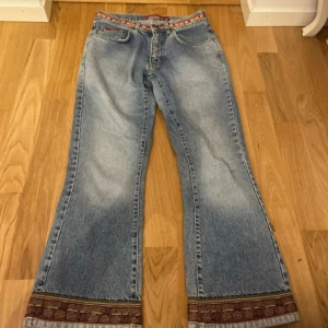 Blå bootcut jeans från ONLY med brodyr - Snygga ljusblå bootcut jeans från ONLY med broderade detaljer i rött och gult vid midjan och benslut. Jeansen har klassisk femficksdesign och är tillverkade i jeansmaterial. Perfekta för dig som vill sticka ut med coola detaljer.