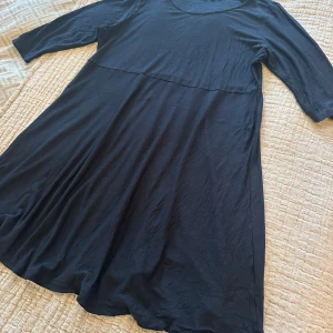 Marinblå klänning från Indiska XL - Marinblå knälångklänning från Indiska i mjukt och lätt viskosmaterial. Klänningen har rund halsringning, trekvartsärm och en enkel, flowy siluett med söm under bysten. Perfekt för dig som gillar minimalistisk stil och vill ha något bekvämt och snyggt.